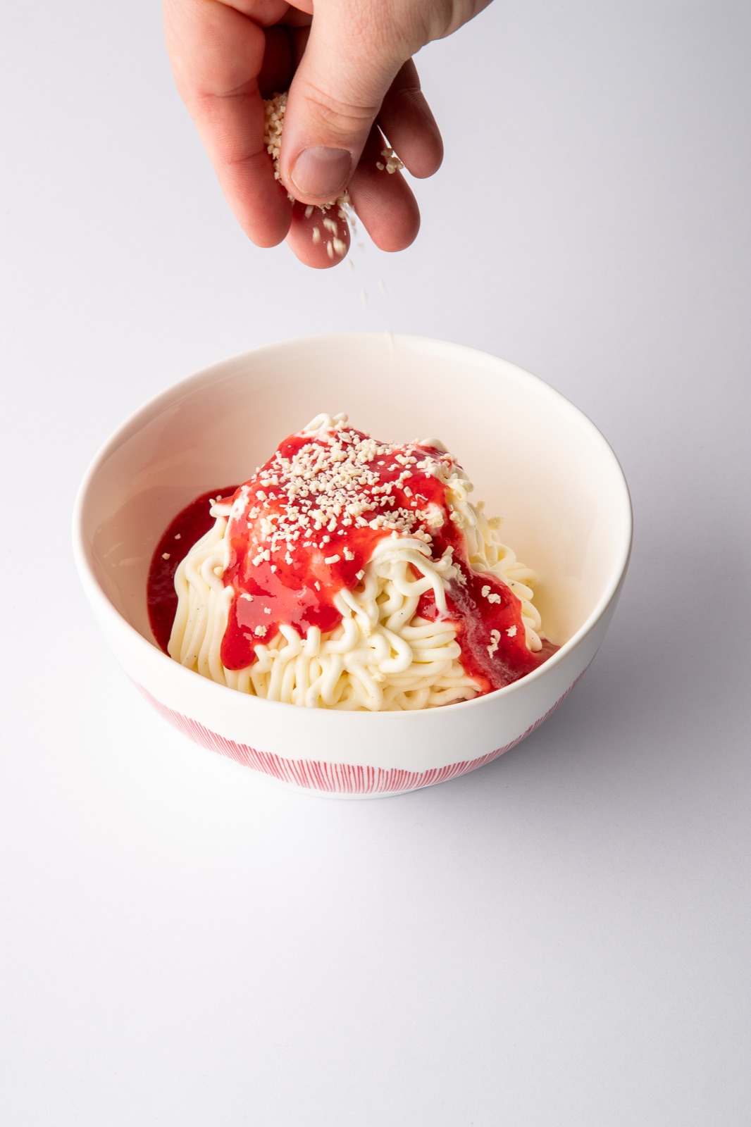 Schlotzeria Spaghetti-Eis mit Erdbeersauce und weißen Schokoraspeln, die per Hand darübergestreut werden
